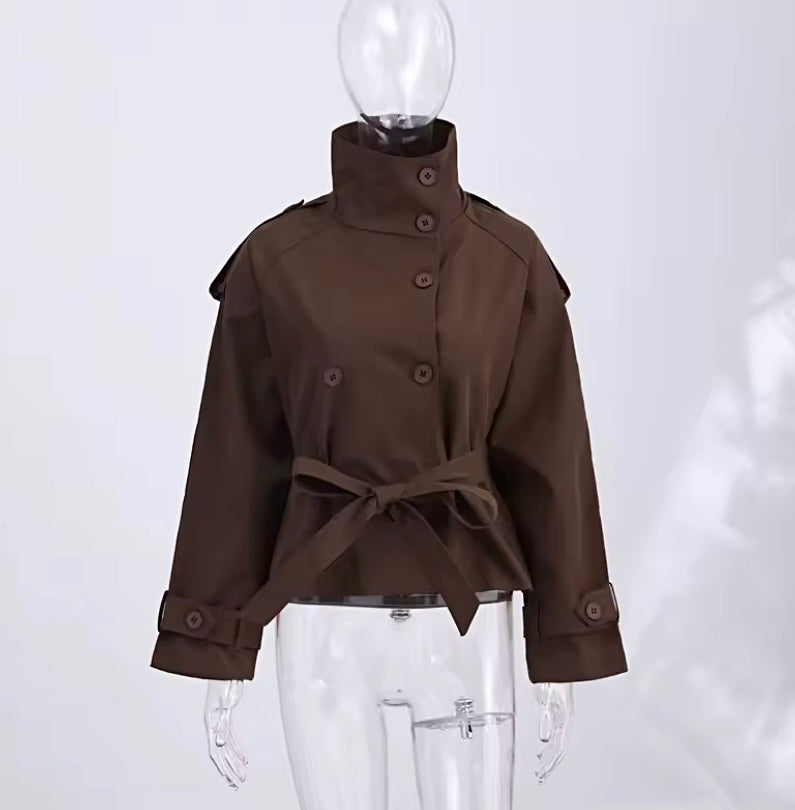 A dark brown cropped trench coat with a high stand collar, button front, shoulder epaulets, and a matching waist tie, displayed on a clear mannequin against a light gray background.