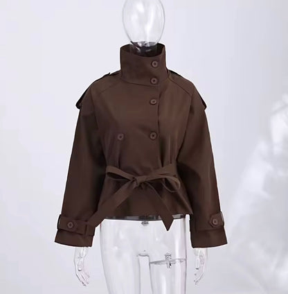 A dark brown cropped trench coat with a high stand collar, button front, shoulder epaulets, and a matching waist tie, displayed on a clear mannequin against a light gray background.