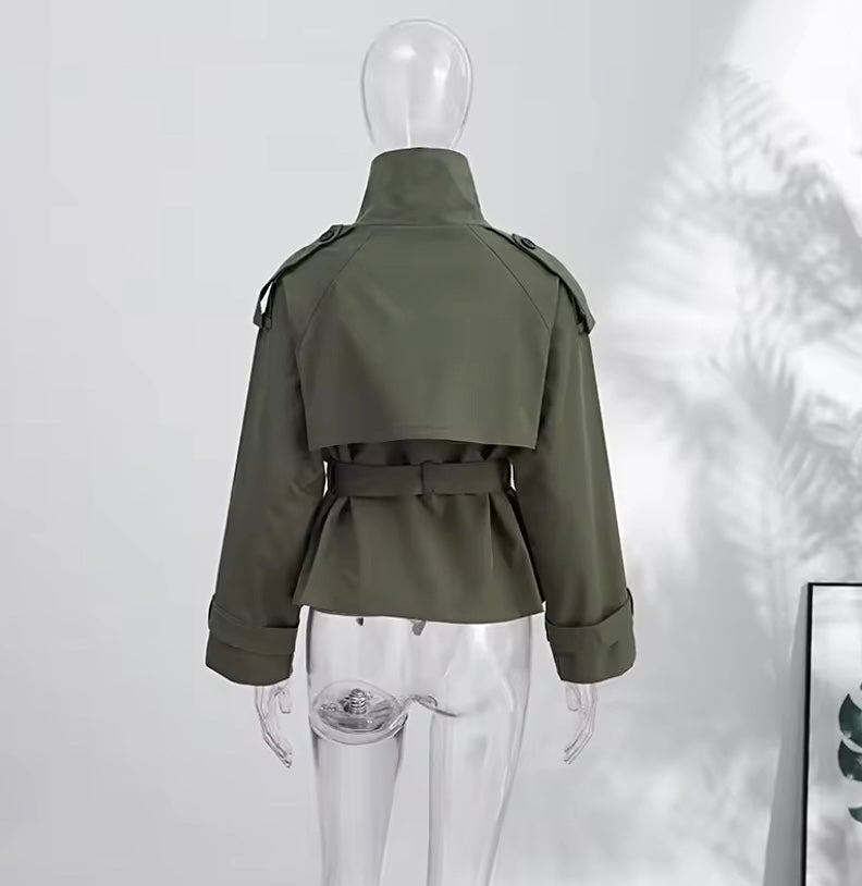 An olive green military-style trench jacket displayed on a clear mannequin from the back, featuring a high collar, shoulder epaulets, and a matching waist belt.